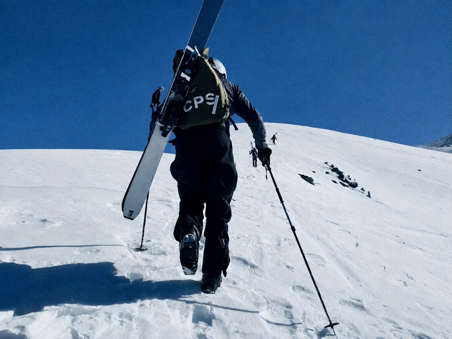 Person foot packing uphill on a snowy mountain with clear blue sky